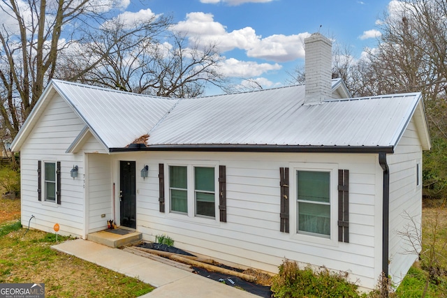 single story home featuring metal roof and a chimney