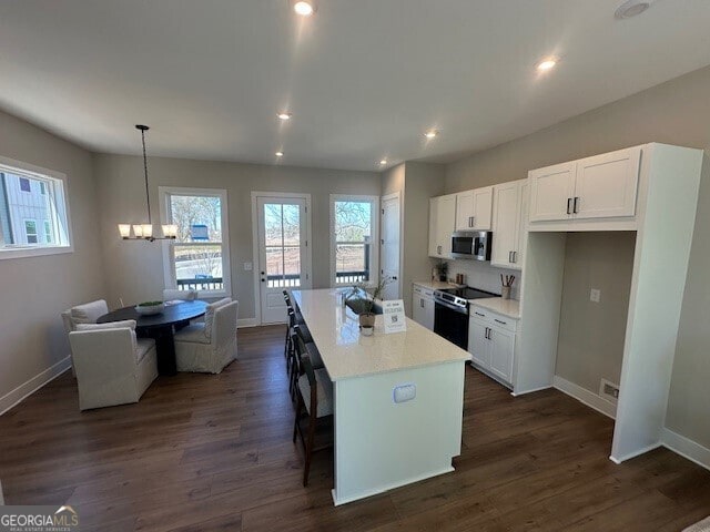 kitchen featuring dark wood finished floors, range with electric stovetop, stainless steel microwave, white cabinetry, and a kitchen island