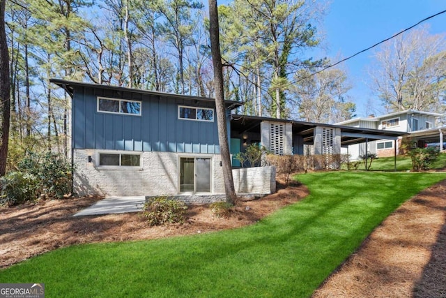 back of house with board and batten siding, a lawn, and brick siding