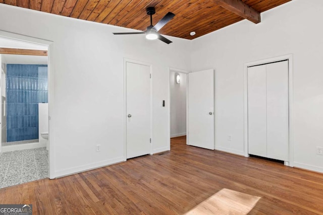 unfurnished bedroom with baseboards, connected bathroom, wood ceiling, wood finished floors, and beam ceiling