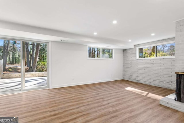 below grade area with light wood-type flooring, brick wall, baseboards, and recessed lighting