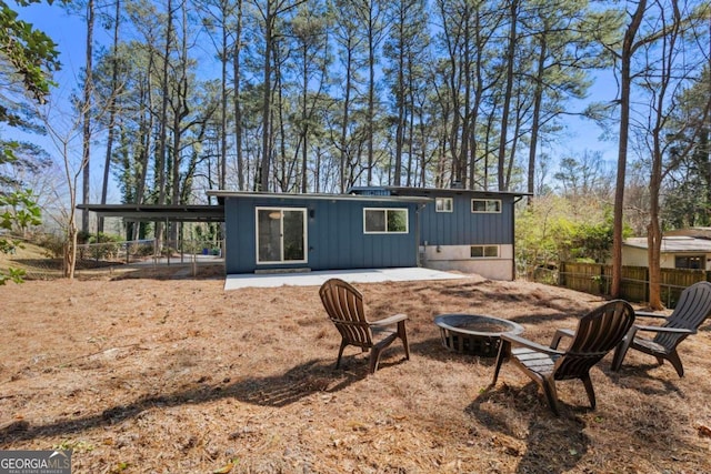 rear view of property with board and batten siding, a patio area, fence, and a fire pit