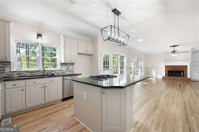 kitchen featuring a sink, light wood-style floors, stainless steel dishwasher, a brick fireplace, and tasteful backsplash