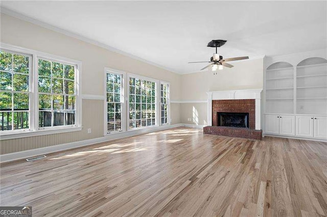 unfurnished living room with built in shelves, a wainscoted wall, visible vents, a brick fireplace, and light wood-type flooring