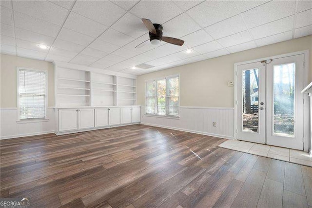 unfurnished room with built in shelves, a wainscoted wall, ceiling fan, and wood finished floors