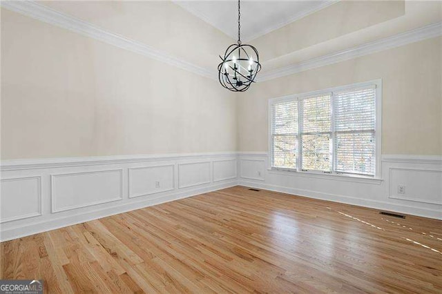 spare room with crown molding, wood finished floors, visible vents, and an inviting chandelier