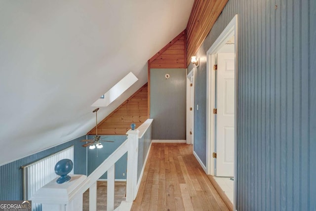 corridor featuring light wood-style floors, vaulted ceiling with skylight, and baseboards