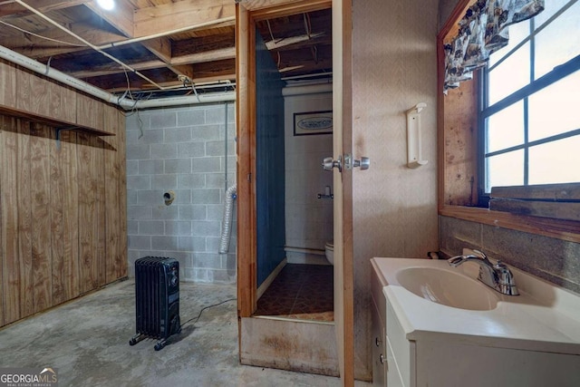 bathroom with concrete block wall, unfinished concrete flooring, vanity, and toilet