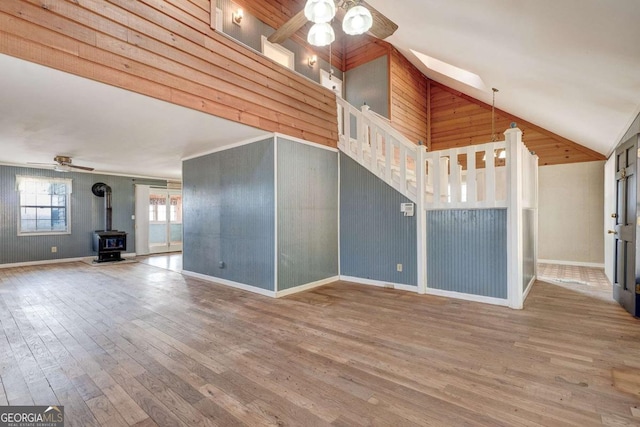 unfurnished living room with a wood stove, ceiling fan, wood finished floors, high vaulted ceiling, and baseboards