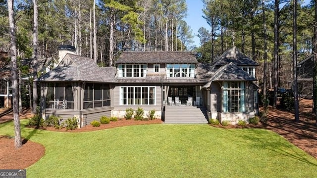 back of property with a chimney, a yard, and a sunroom