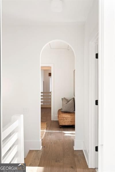 hall featuring baseboards, arched walkways, and wood finished floors