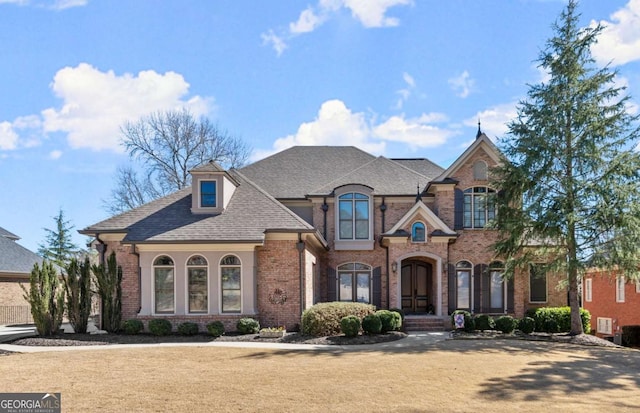 french provincial home featuring brick siding and a shingled roof