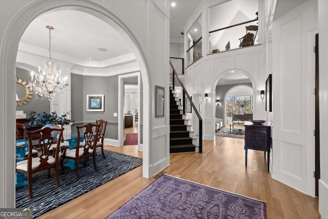 entrance foyer with stairway, wood finished floors, arched walkways, crown molding, and a notable chandelier