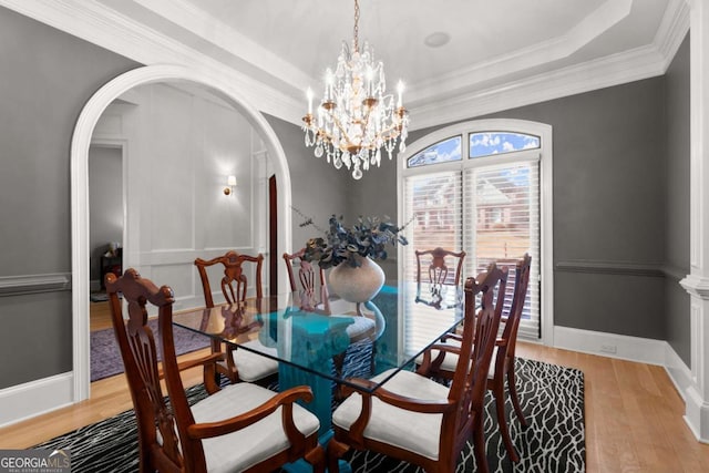 dining area with ornamental molding, a tray ceiling, wood finished floors, arched walkways, and baseboards