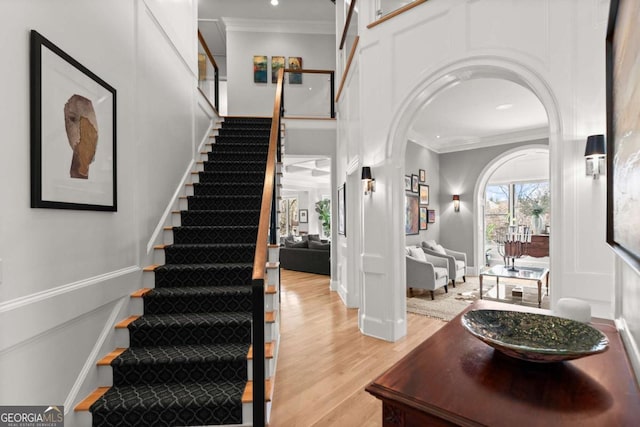 entrance foyer featuring stairs, crown molding, arched walkways, and light wood-type flooring