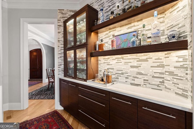 bar featuring tasteful backsplash, crown molding, baseboards, light wood-type flooring, and arched walkways