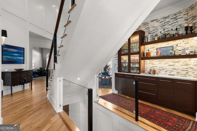 bar featuring wet bar, stairway, light wood-style floors, and backsplash