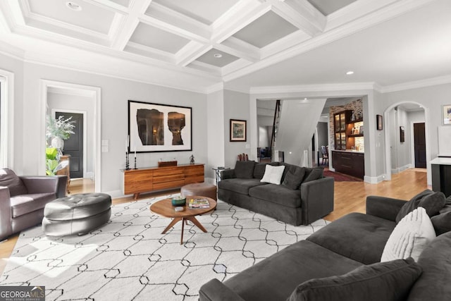 living room with coffered ceiling, light wood finished floors, beam ceiling, arched walkways, and ornamental molding