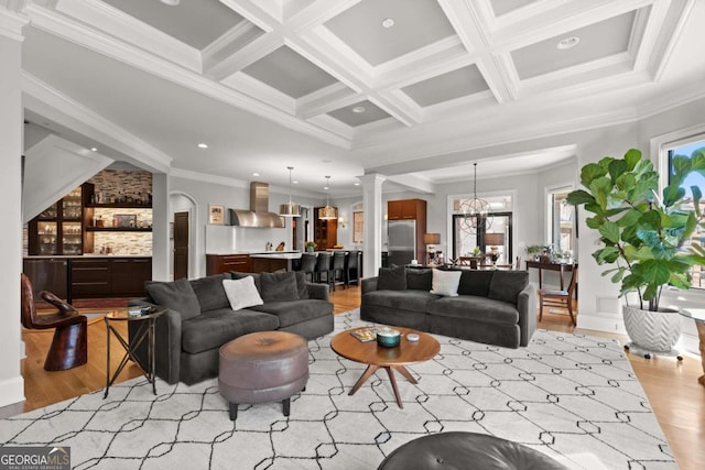 living room featuring crown molding, light wood finished floors, coffered ceiling, and ornate columns