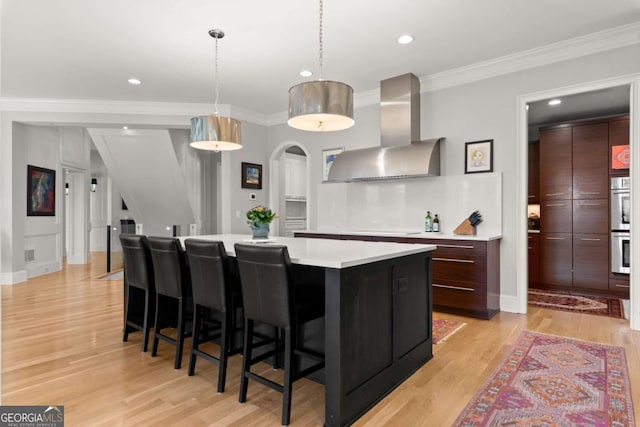 kitchen featuring light countertops, a large island, light wood-style floors, wall chimney exhaust hood, and modern cabinets