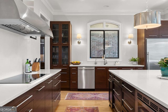 kitchen featuring range hood, light countertops, built in appliances, and ornamental molding