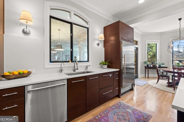 kitchen featuring a sink, stainless steel appliances, light countertops, crown molding, and light wood-type flooring