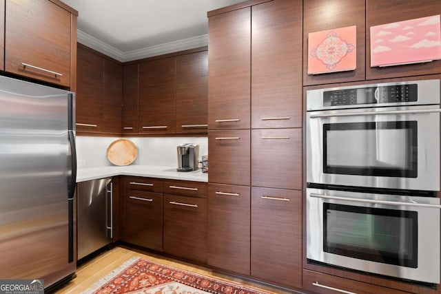 kitchen with ornamental molding, stainless steel appliances, dark brown cabinetry, light wood finished floors, and light countertops