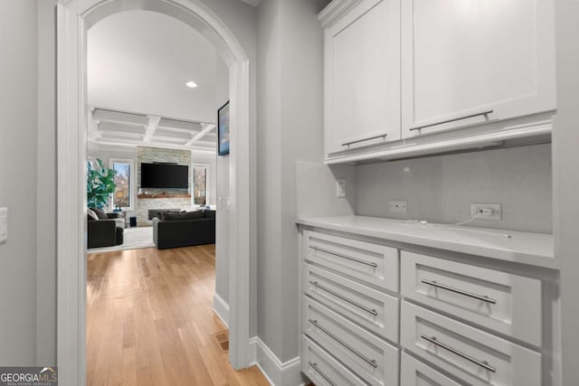 corridor featuring baseboards, coffered ceiling, arched walkways, beamed ceiling, and light wood-type flooring