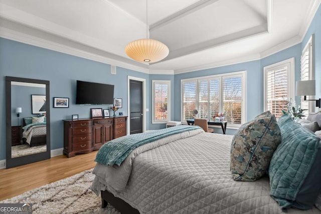 bedroom featuring a tray ceiling, crown molding, wood finished floors, and baseboards