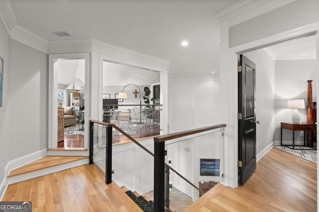 corridor featuring baseboards, an upstairs landing, light wood-type flooring, and ornamental molding