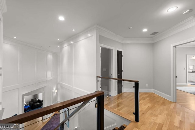 corridor featuring an upstairs landing, a decorative wall, light wood finished floors, and crown molding