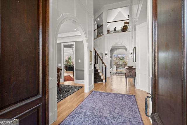 foyer featuring crown molding, light wood-style flooring, stairway, and arched walkways