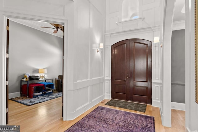 entryway with a ceiling fan, a decorative wall, wood finished floors, and ornamental molding