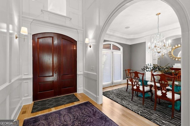 entrance foyer featuring a decorative wall, arched walkways, light wood finished floors, and ornamental molding