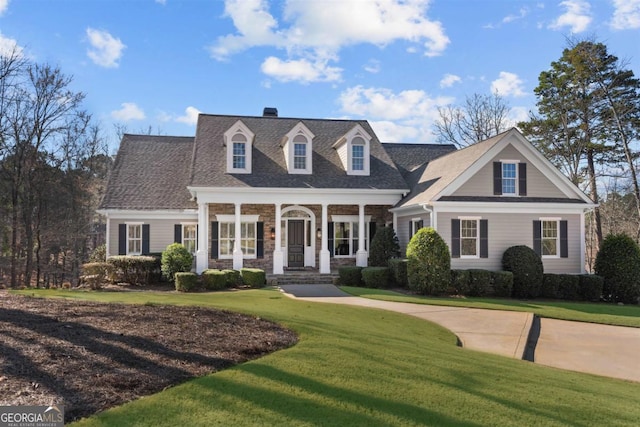 view of front of property with covered porch, stone siding, a front lawn, and roof with shingles