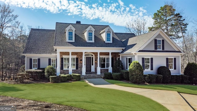 cape cod-style house with stone siding, a porch, roof with shingles, and a front yard