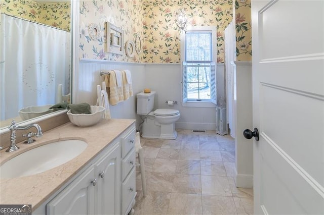 bathroom featuring wallpapered walls, a shower with shower curtain, toilet, a wainscoted wall, and vanity