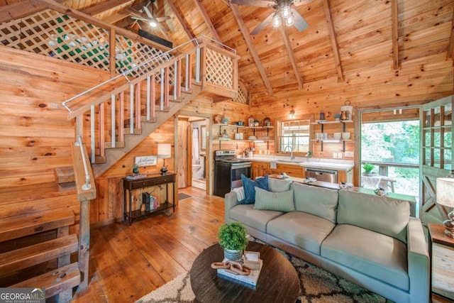 living area with ceiling fan, wooden walls, wood ceiling, light wood-style floors, and beamed ceiling