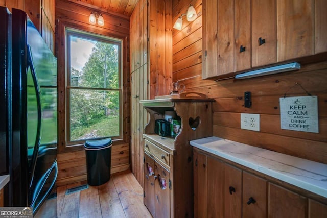 interior space featuring brown cabinetry, wood walls, freestanding refrigerator, and light wood-style floors