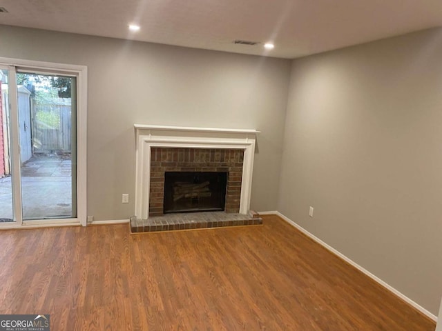 unfurnished living room featuring a brick fireplace, baseboards, wood finished floors, and recessed lighting