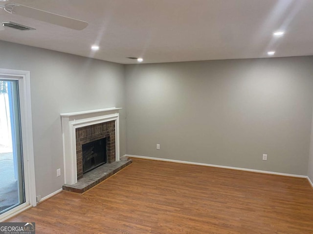 unfurnished living room with a brick fireplace, wood finished floors, visible vents, and recessed lighting