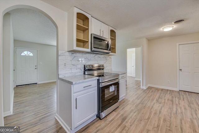 kitchen featuring arched walkways, light wood-style flooring, visible vents, white cabinetry, and appliances with stainless steel finishes