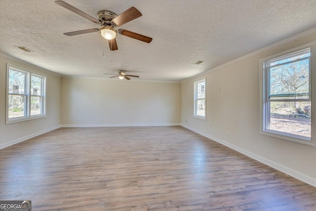 empty room featuring a textured ceiling, wood finished floors, visible vents, baseboards, and ornamental molding