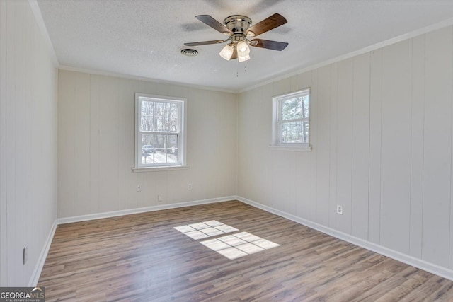 empty room with a textured ceiling, wood finished floors, visible vents, and a ceiling fan