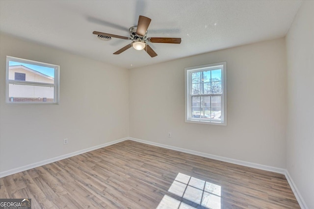 empty room with a textured ceiling, ceiling fan, light wood finished floors, and baseboards