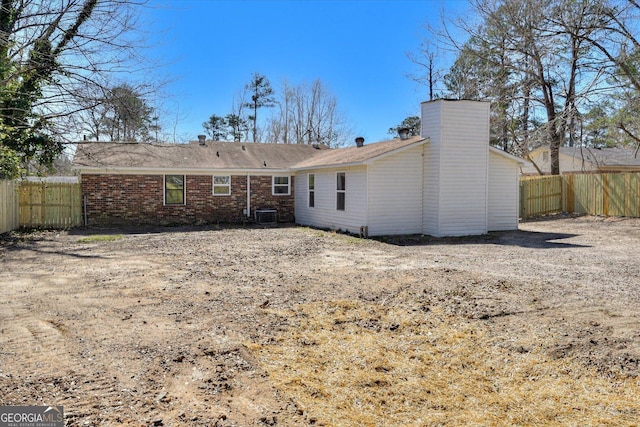 back of property featuring central AC, brick siding, fence, and a chimney