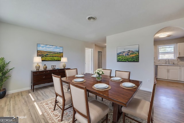 dining space with arched walkways, baseboards, visible vents, and light wood-style floors