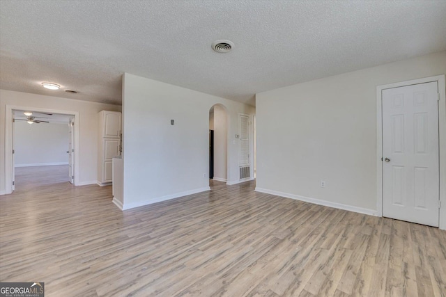 empty room featuring arched walkways, a textured ceiling, light wood-style flooring, visible vents, and baseboards