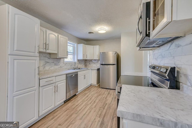 kitchen featuring white cabinets, appliances with stainless steel finishes, light countertops, light wood-style floors, and a sink