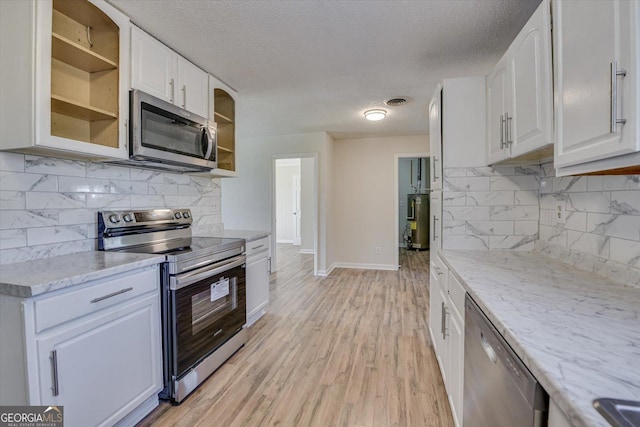 kitchen with light wood-style flooring, stainless steel appliances, white cabinetry, water heater, and glass insert cabinets